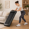 Woman moving a folding walking pad into upright storage beside a sofa