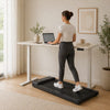 Woman using an under-desk walking pad beneath a standing desk in a home office