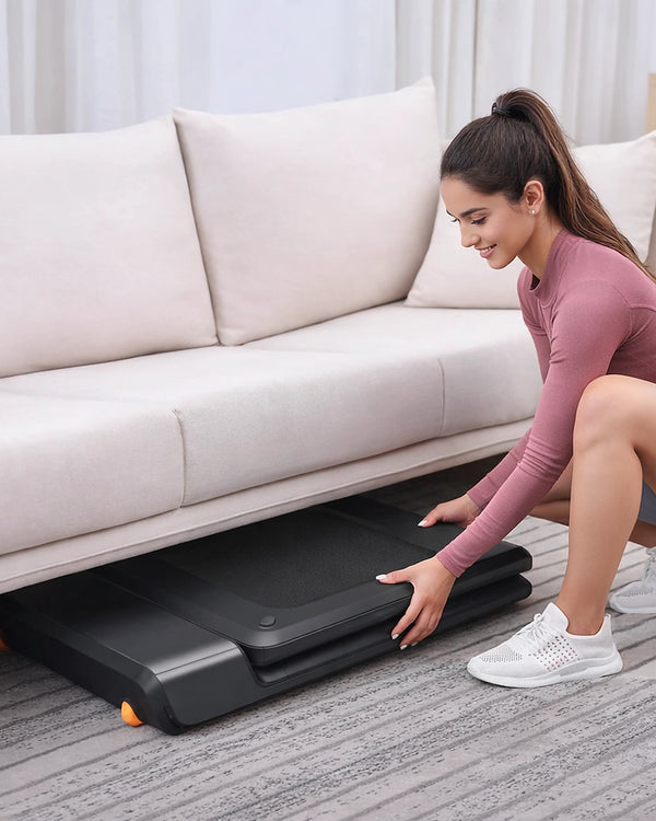 Woman storing WalkingPad A1 Pro folded treadmill under a sofa in a UK living room