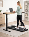 Woman using WalkingPad A1 Pro under a standing desk in a bright UK home office